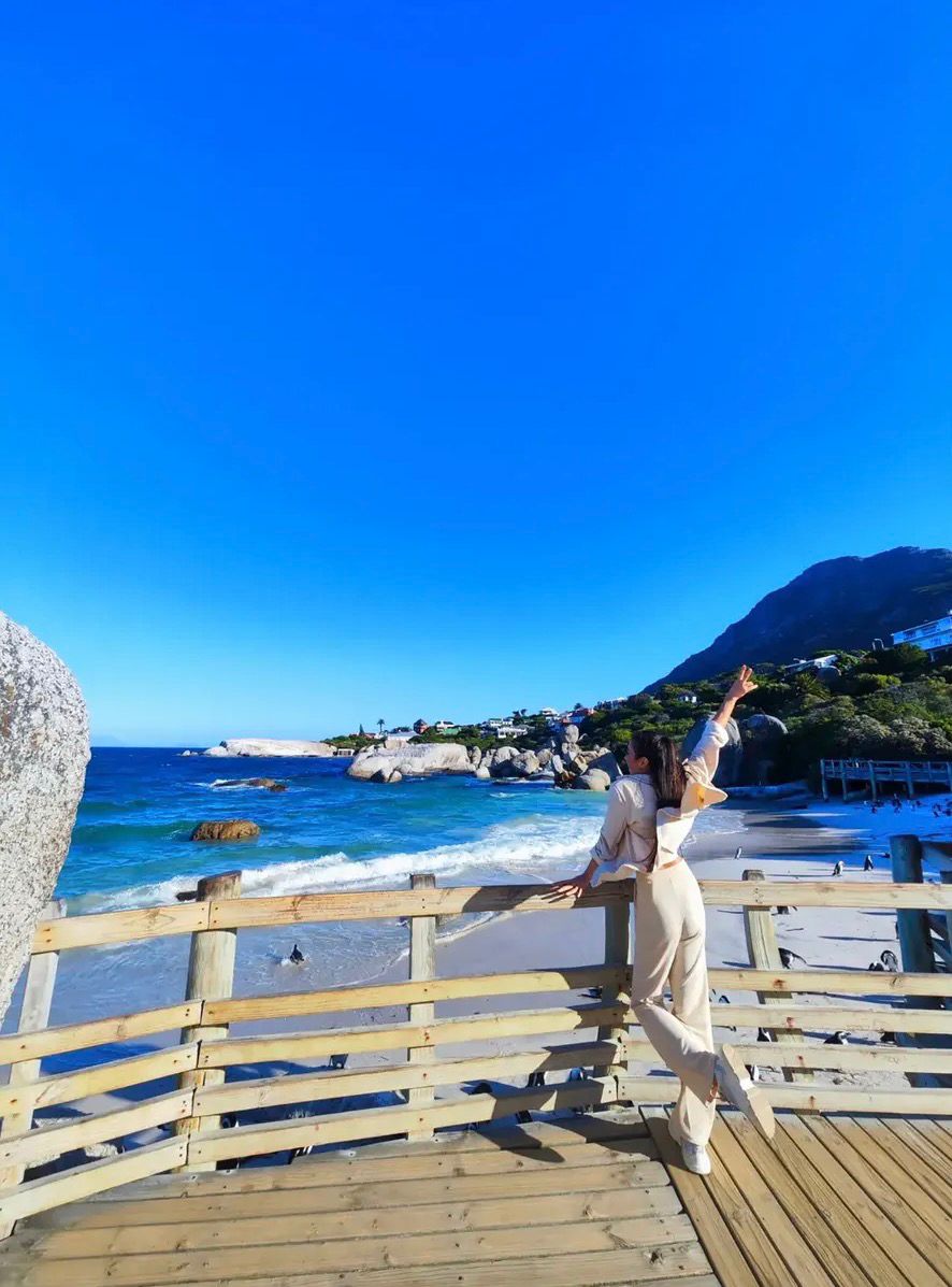 Alexandra, co-founder of The Wild Table, in cream linen on a wooden boardwalk above the sea