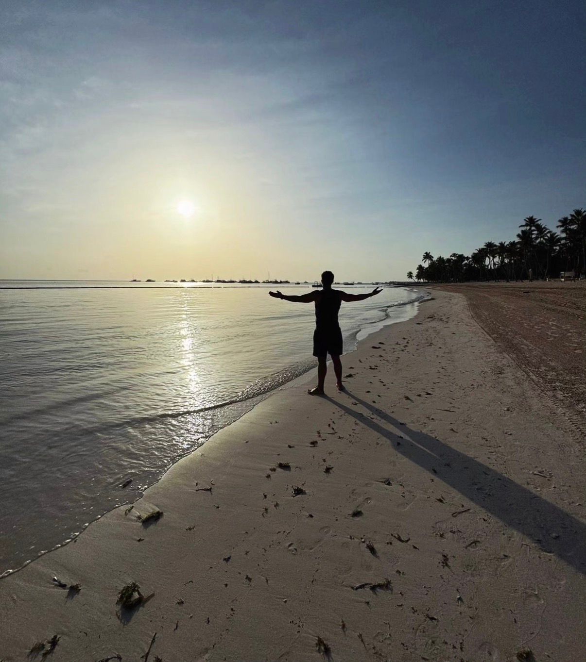 Omar, co-founder of The Wild Table, silhouetted with arms outstretched on a beach at golden hour